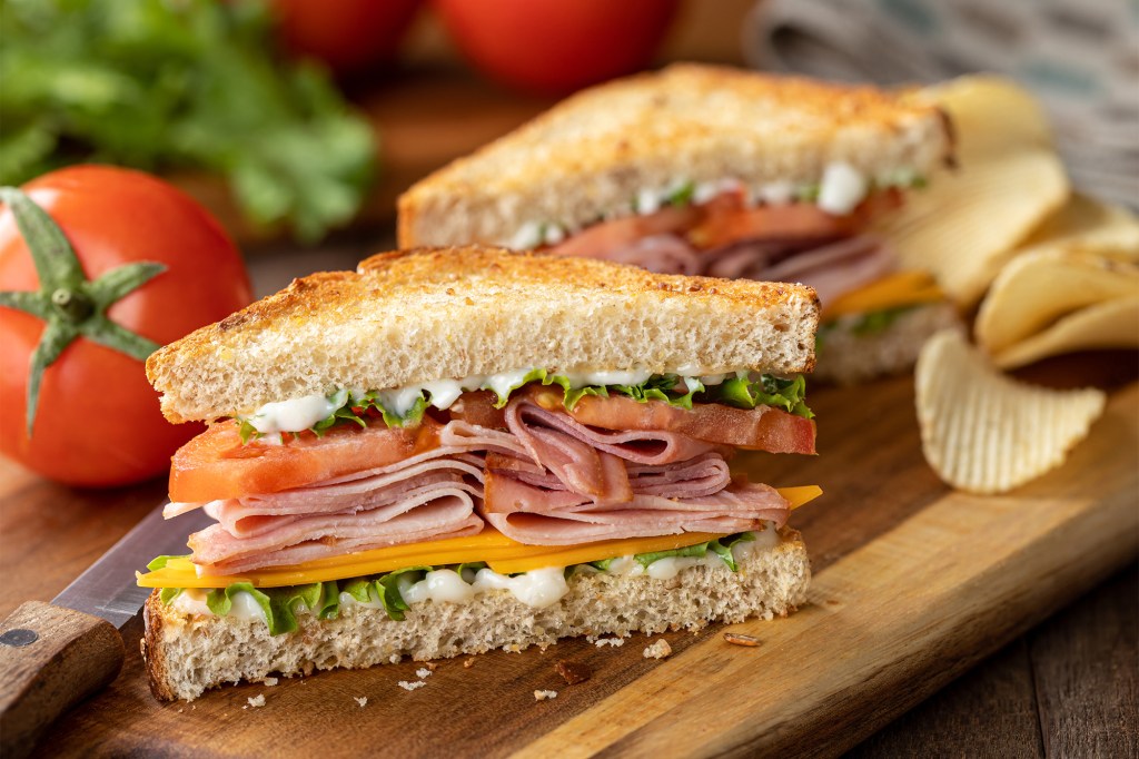 A chef prepares a sandwich on a cutting board with dried vegetables and an oil-based coating to avoid moisture